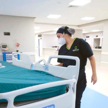 Enfermera con mascarilla revisando una cama de hospital.