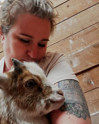 Person with a tattoo cuddling a small goat indoors.