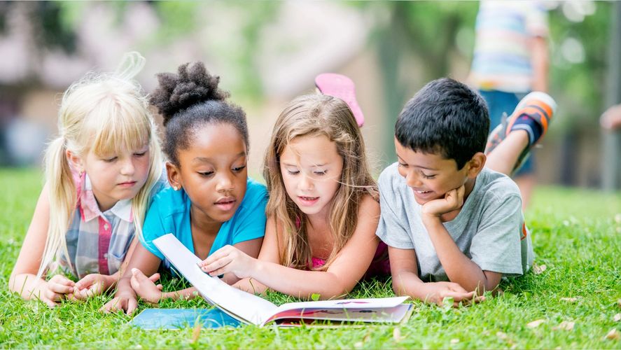 Four Kids laying on their stomachs looking at a book.