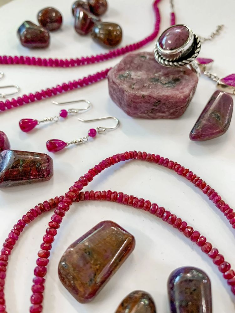 Ruby and sapphire jewelry, specimen, and tumbled pieces on a white background.