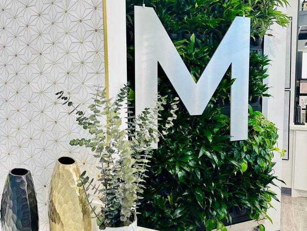 Gold and white tile Spa at M logo on lush live greenery wall. To remove imurities from the spa.