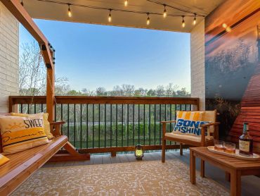 Cozy porch with wooden swing, string lights, and scenic view of trees and river at Sunny Side Falls