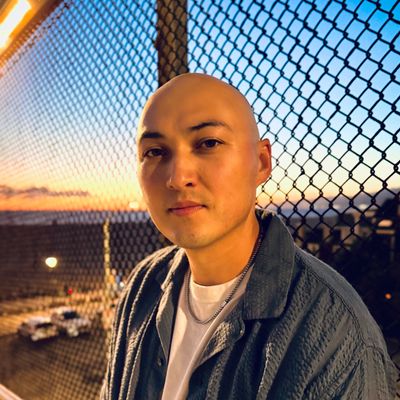 Man posing near chain-link fence at sunset.