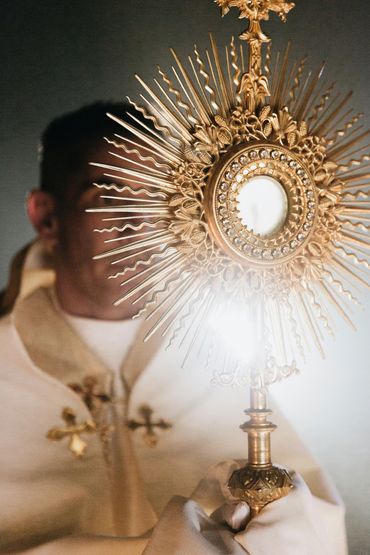 A priest holding a golden monstrance with a shining light in a religious ceremony.