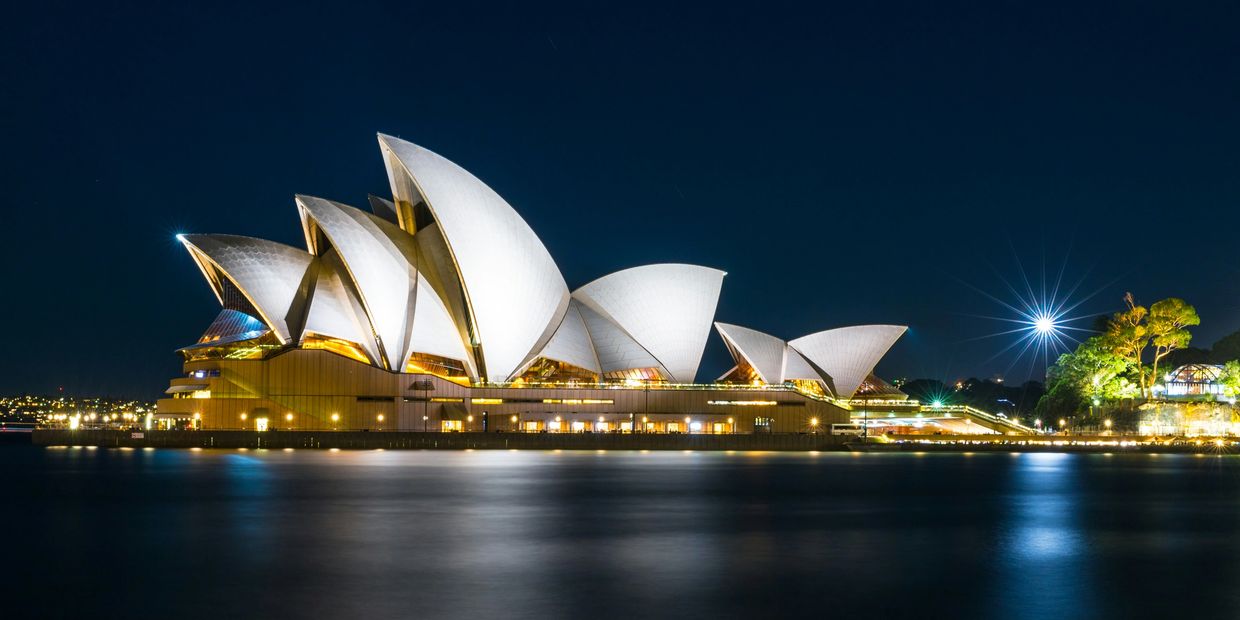 Sydney Opera House illuminated at night by the water.
