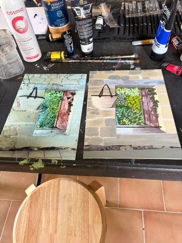 Two paintings of outside shutter windows in a tobacco barn with greenery on a table, surrounded by art supplies.
