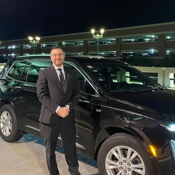 the owner of white sands transportation stands next to an executive sedan drop off at the airport
