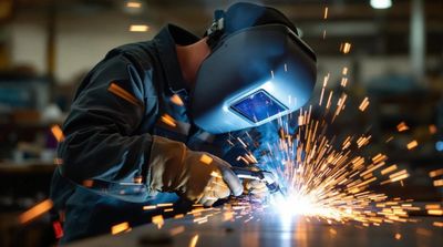 A welder in protective gear sparks bright light while welding metal.