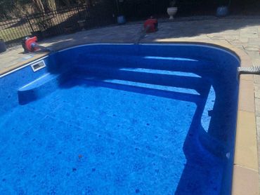 Empty blue pool with cleaning equipment around it on a sunny day.