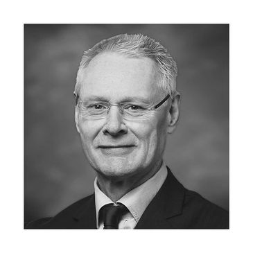 Portrait of a mature man in a suit and glasses against a blue background.