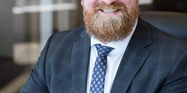Smiling man in suit with beard and patterned tie.