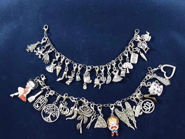 Two charm bracelets with various silver charms on a dark blue background.