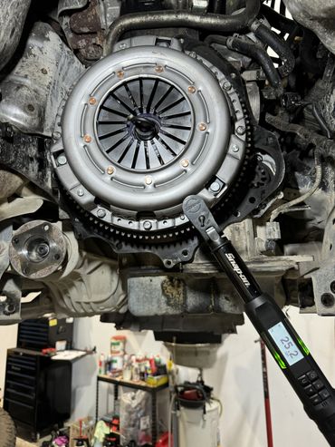 A torque wrench tightening a car clutch assembly in a garage.