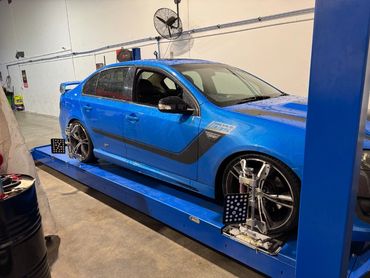 Blue sports sedan on alignment platform with wheel sensors attached.