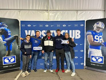 Group of five people posing in front of a Varsity Club BYU backdrop.