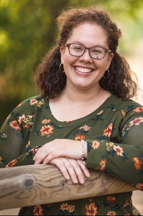 Smiling woman in floral green top leaning on a wooden railing outdoors.