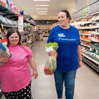 Two women grocery shopping, one holding pasta and the other fresh vegetables.