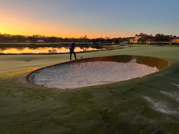 Sunset over a golf course with a man edging a bunker.