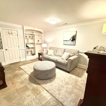 Cozy living room with beige sofa, round ottoman, and soft lighting.