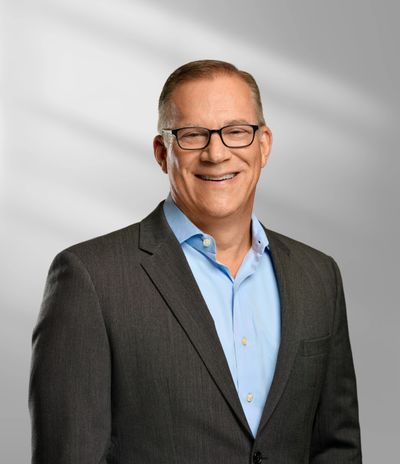 Smiling middle-aged man in glasses wearing a dark suit and light blue shirt.