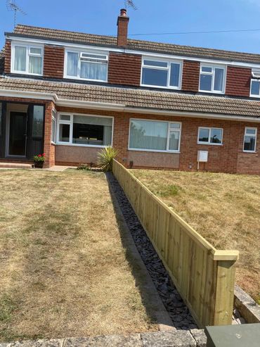 A semi-detached house with a wooden fence separating two dry lawns.