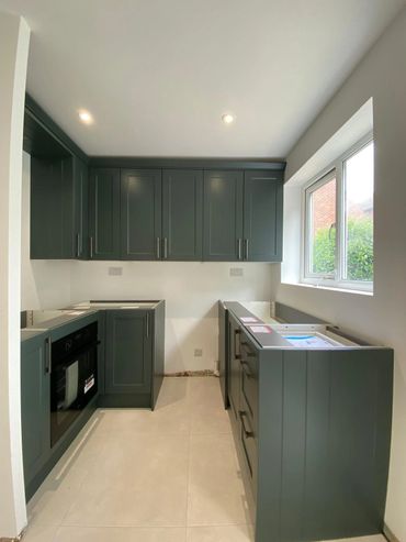 Modern green kitchen cabinets being installed with natural light from the window.