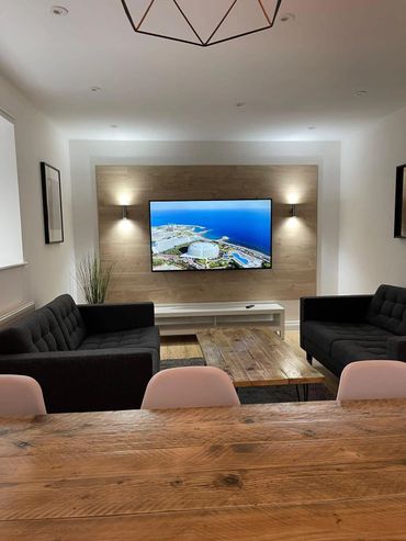 Modern living room with black sofas, wooden coffee table, and wall-mounted TV.
