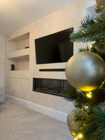 Modern living room with mounted TV, fireplace, and decorated Christmas tree.