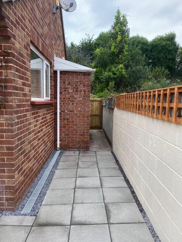 A paved backyard path with brick walls and a wooden gate at the end.