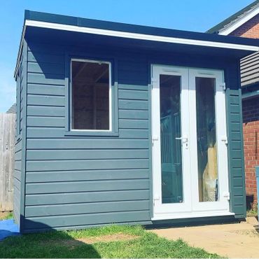Modern garden shed with blue siding and white-framed glass doors and window.