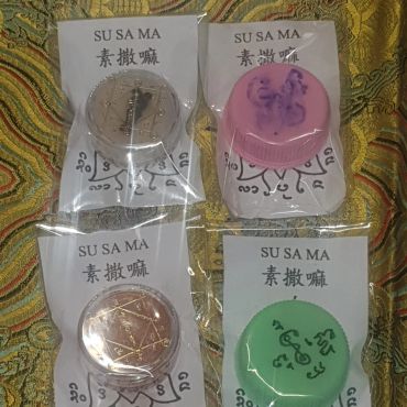 Four colored circular amulets in plastic bags on a patterned cloth.