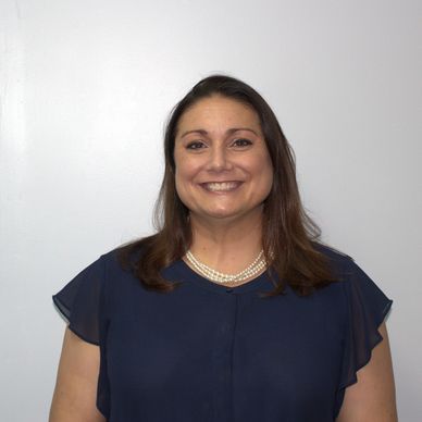 Smiling woman in a navy blouse and pearl necklace against a plain background.