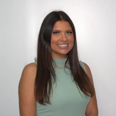 Smiling woman with long dark hair wearing a sleeveless mint green top.