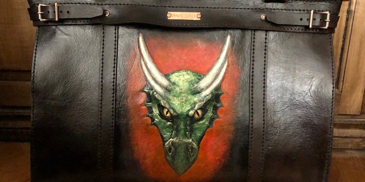 Black leather bag with a fierce green dragon head painted on it.