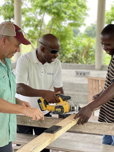Three men working together on a woodworking project outdoors.