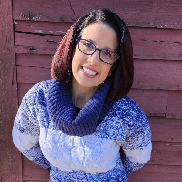 Woman smiling in a blue and white sweater against a wooden wall.