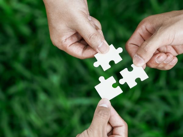 Three hands connecting white puzzle pieces together.