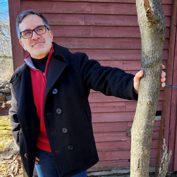 Man in glasses and coat holding a tree trunk outdoors.