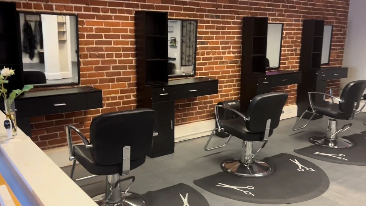 Modern hair salon chairs and stations with brick wall backdrop.