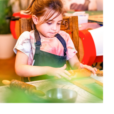 Young girl focused on rolling dough with a wooden rolling pin.