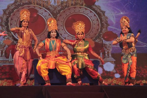 Four dancers in traditional Indian attire performing on stage with vibrant backdrop.