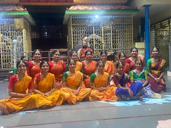 Group of dancers in traditional Indian attire posing in a temple setting.