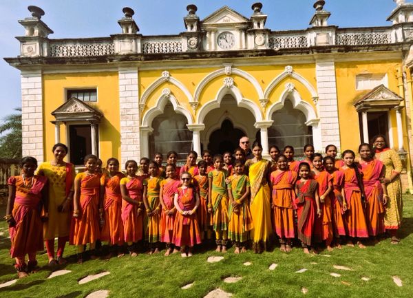 Group of girls and teachers in traditional attire standing in front of a historic building.