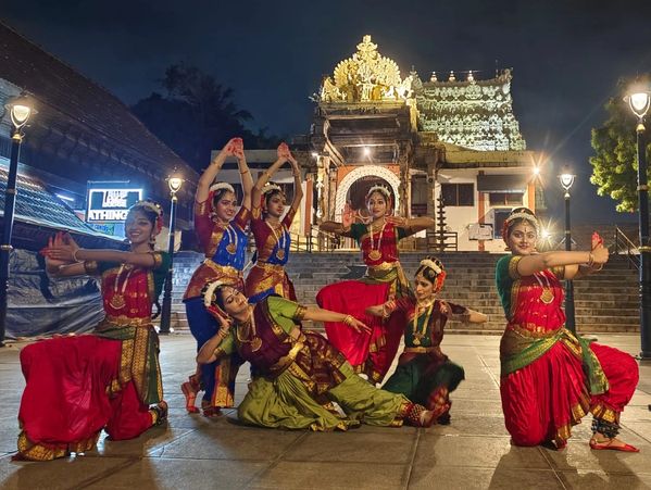 Group of classical dancers posing in traditional attire at night in front of a temple.