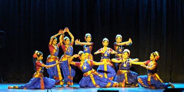 Group of dancers in traditional blue and gold attire performing on stage.