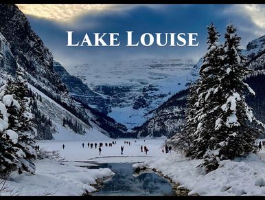 A stream leading to the frozen Lake Louise with people skating and snow covered mountains.