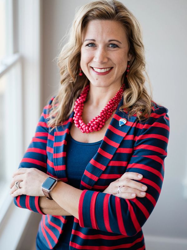 Brooke Sines in a red and navy striped suit coat with a RE/MAX balloon lapel pin on the lapel