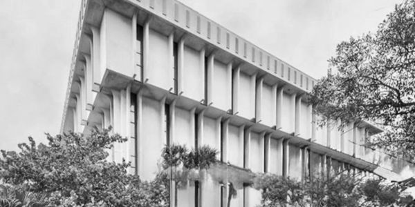 A modernist white concrete building surrounded by trees under a cloudy sky.