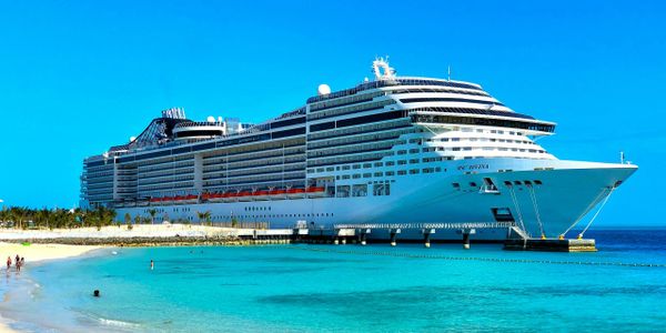 Large cruise ship docked at a tropical beach with clear blue water.