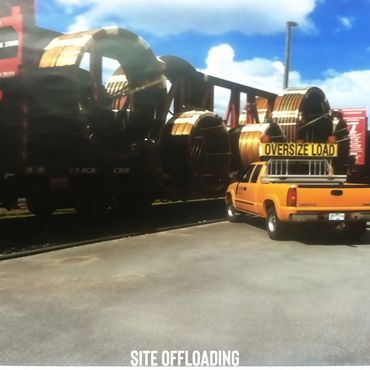 Yellow truck with oversize load sign next to large industrial equipment on a sunny day.